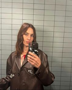 a woman taking a selfie with her cell phone in front of a tiled wall