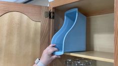 a person holding a blue object in front of a wooden shelf with glasses on it