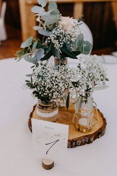 flowers and greenery are in mason jars on a wood slice for centerpieces