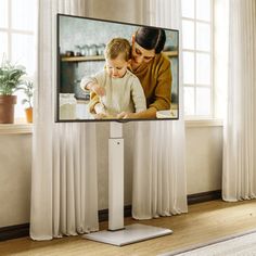 a woman holding a baby in front of a flat screen tv with the image of a mother and child on it