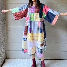 a woman standing in front of a wall wearing a colorful dress with patches on it