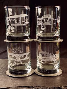 three glass tumblers sitting on top of a wooden table with an airplane etched on them