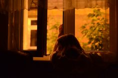 a woman sitting in front of a window with her hands up to the window sill