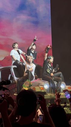 group of people sitting on the back of a car in front of a large screen