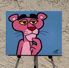 a painting of a pink cat with yellow eyes on a blue and white background by a easel