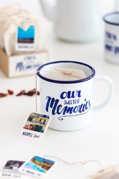 a white coffee mug with blue lettering on it next to some other cups and tags