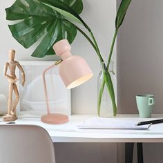 a pink lamp on a desk next to a vase with a green plant in it