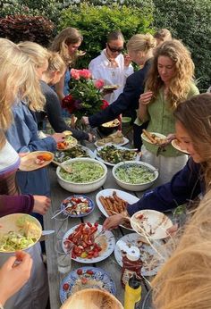 a group of people standing around a table filled with plates and bowls full of food