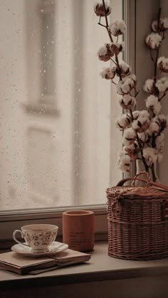 a cup and saucer sitting on a window sill next to a basket with cotton flowers