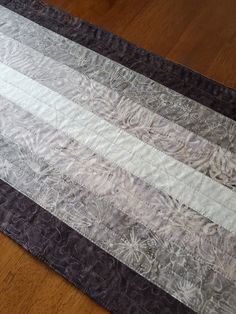 a close up of a quilt on a wooden floor with a black and white stripe