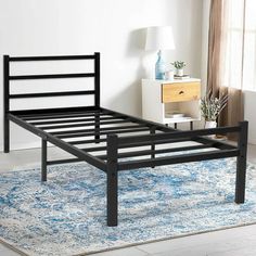 a black metal bed frame on top of a blue rug in a room with white walls