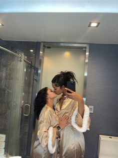 two women are kissing in the bathroom while taking a selfie with their cell phone