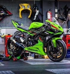 a green and black motorcycle parked in a garage next to some tools on the ground