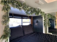 a bed with black sheets and pillows in a room that has plants growing on the wall