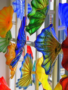 colorful glass art hanging from the side of a window in front of a white wall