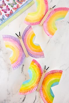 four paper plate rainbows with clothes pins sticking out of them on a marble surface