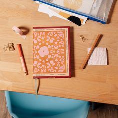 an open notebook sitting on top of a wooden table next to some pens and pencils