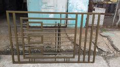 a metal gate sitting on the side of a road next to a blue building and a trash can