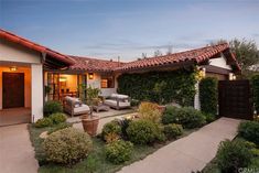 an outdoor patio with chairs and plants in the foreground, next to a house