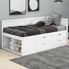 a white bed with drawers underneath it in a room next to a rug and pictures on the wall