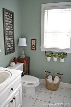 a white toilet sitting next to a sink in a bathroom under a window with potted plants