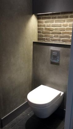 a white toilet sitting in a bathroom next to a brick wall