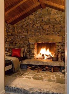 a stone fireplace in the middle of a room with a bed and pillows on it