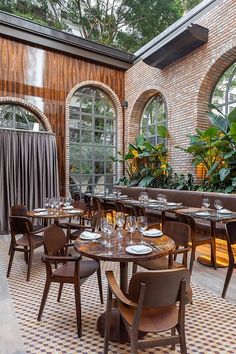 a dining room with tables and chairs in front of large arched windows, surrounded by greenery