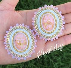 pair of pink and gold earrings on hand with grass in the backgroung