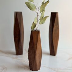 three wooden vases with plants in them on a marble countertop, one is made out of wood and the other has green leaves