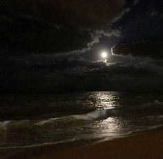 the moon is setting over the ocean with waves coming in to shore and dark clouds