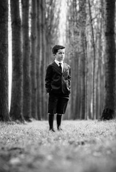 a young boy standing in the middle of a forest wearing a suit and tie with his hands on his hips