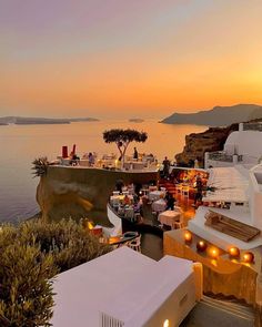 an outdoor dining area overlooking the ocean at sunset with lights lit up on tables and chairs