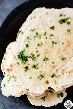 three flat breads on a black plate with parsley sprinkled on top