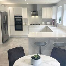 a white kitchen with an island table and chairs next to the stove top oven in the center