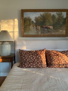 a bed with two pillows and a painting on the wall above it, along with a lamp