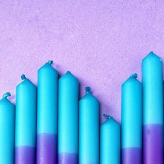 blue and purple candles are lined up on a pink surface with one candle in the middle