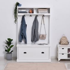 a white coat rack with two coats hanging on it's sides and a potted plant next to it