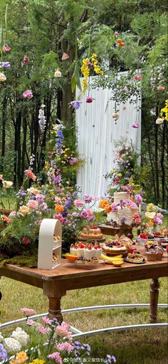 an outdoor table with flowers and cake on it in the middle of a garden area