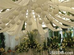 a room filled with lots of white flowers and hanging balls over the top of it