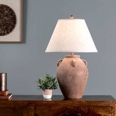 a table lamp sitting on top of a wooden dresser next to a potted plant