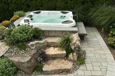 an outdoor hot tub surrounded by rocks and plants