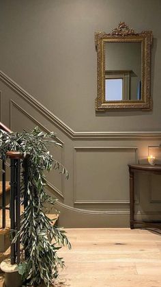 a plant sitting on top of a wooden floor next to a stair case with a mirror above it