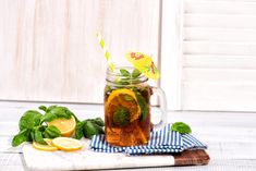 a glass mug filled with tea next to lemons and mint leaves on a cutting board