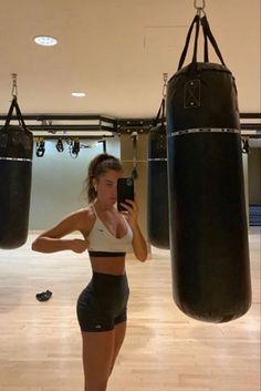 a woman taking a selfie with her cell phone in a boxing ring while standing next to two punching bags