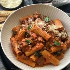 a white bowl filled with pasta and sauce on top of a table next to bread