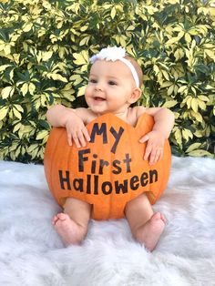 a baby sitting on top of a pumpkin with the words my first halloween written on it