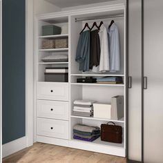 a white closet with drawers and clothes hanging on the wall, next to a door