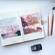 an open notebook with watercolors and pencils next to it