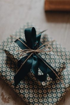 a wrapped gift box with a black bow on it sitting on top of a wooden table